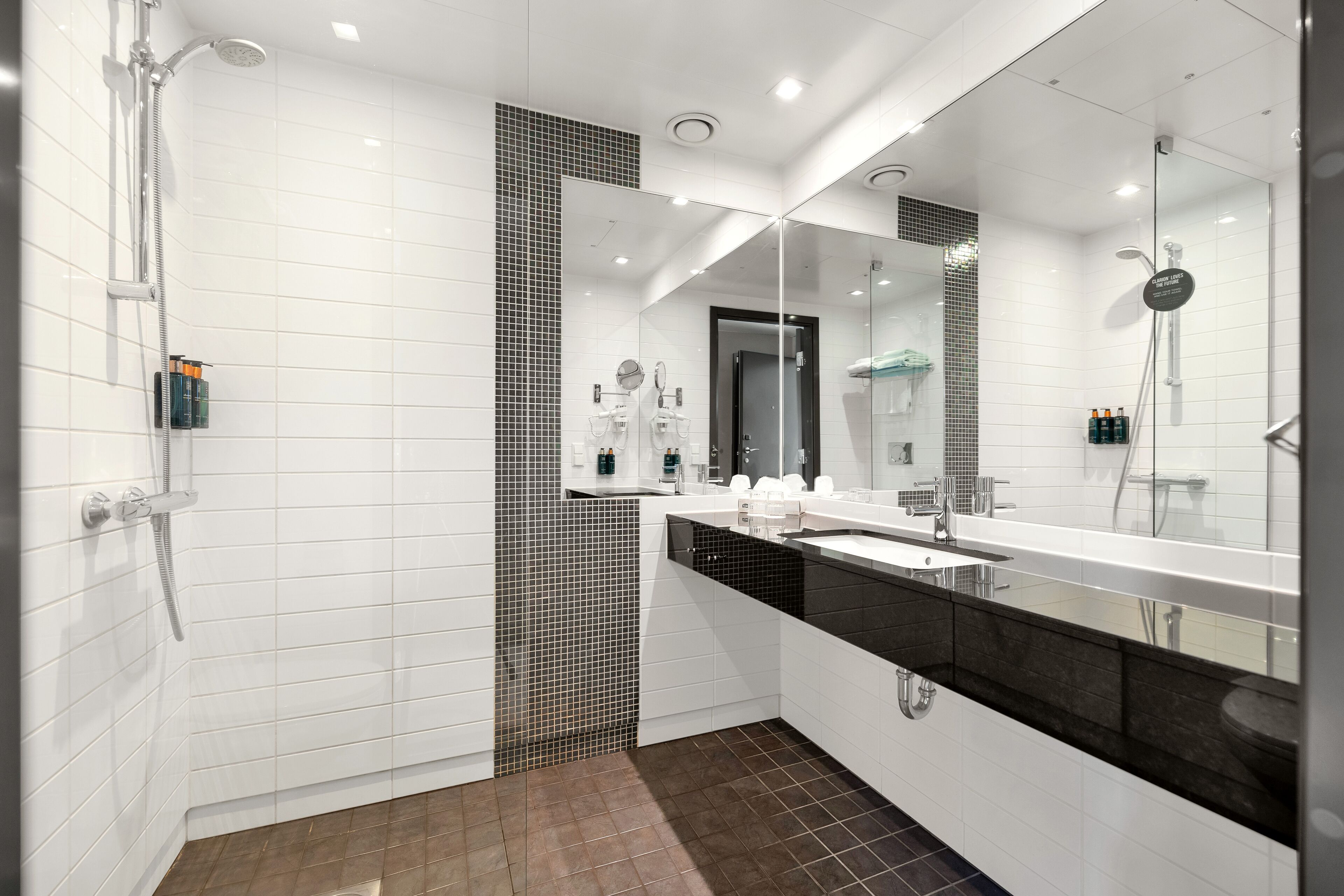 Een moderne badkamer met een glazen douchecabine, witte betegelde wanden, een zwart aanrecht en een grote spiegel.