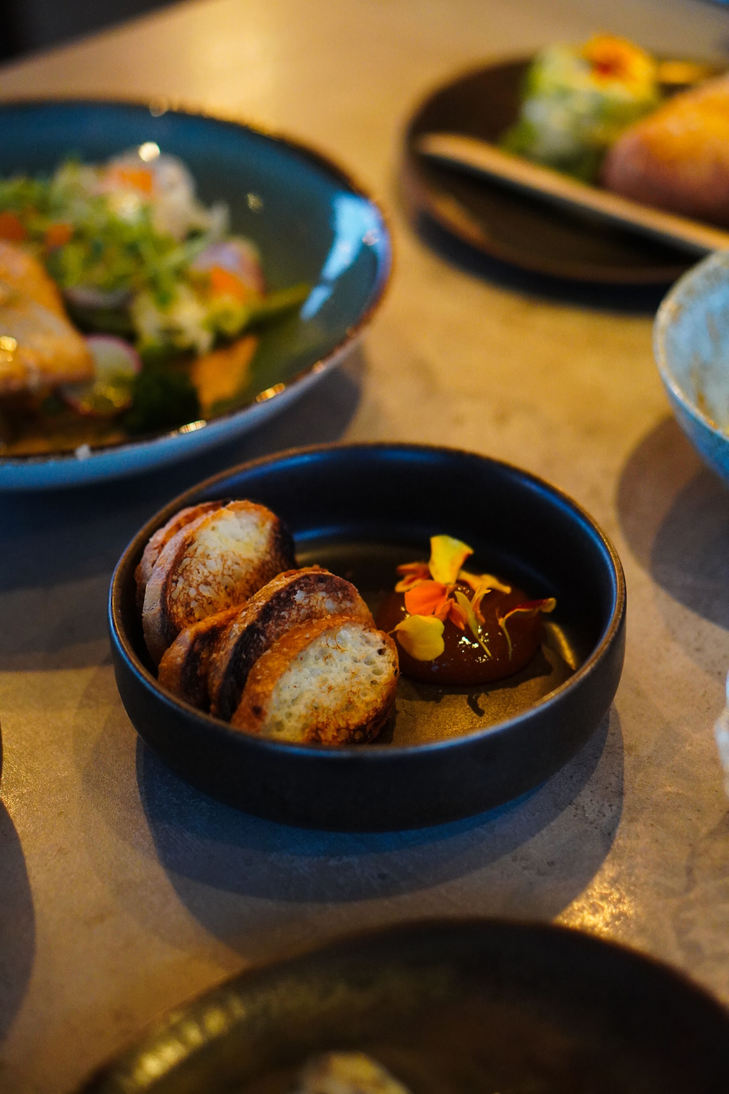 Una mesa con varios platos, incluyendo un bol de pan en rodajas y un bol de sopa con guarnición.