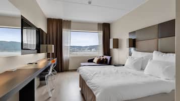 A modern hotel room with a large bed, a desk with a chair, a TV, and a view of a cityscape.