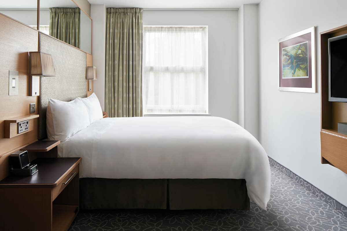 Ein Hotelzimmer mit einem großen Bett, einem Schreibtisch mit Telefon, einem Fernseher und einem Fenster mit Vorhängen.