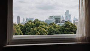 A city skyline through a window with a view of modern buildings and dense green trees.
