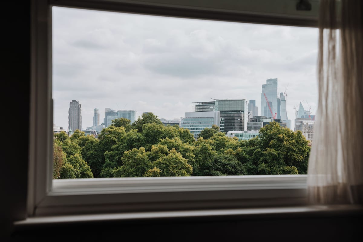 Blick aus einem Fenster auf einen Stadtpanoramablick mit modernen Gebäuden und üppigen Grünflächen.