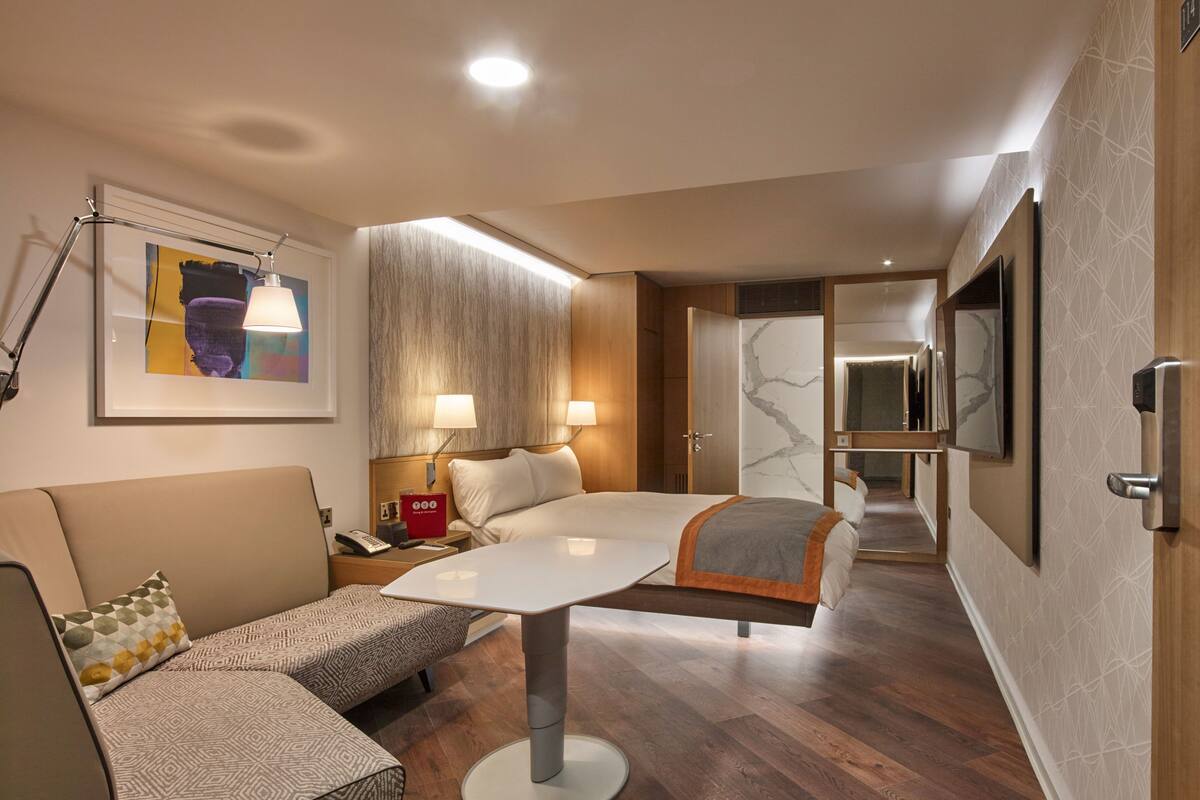 Ein modernes Hotelzimmer mit einem großen Bett, einer Couch, einem Esstisch und einem an der Wand befestigten Fernseher.