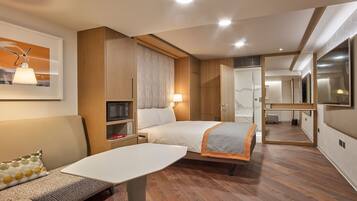A modern hotel room with a bed, a sofa, a small table, a microwave, and a mirror.
