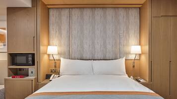 Una habitación de hotel con una cama grande, dos lámparas de noche, un microondas, un teléfono y un mueble pequeño.