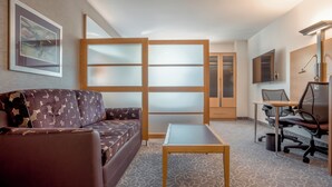 A modern hotel room with a sofa, a small table, a desk with a chair, a TV, and a sliding door.