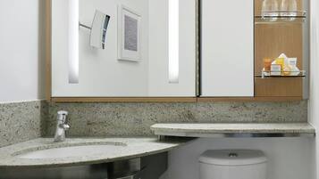 A modern bathroom with a granite countertop, a stainless steel sink, a mirror, a framed picture, and a shelf with toiletries.