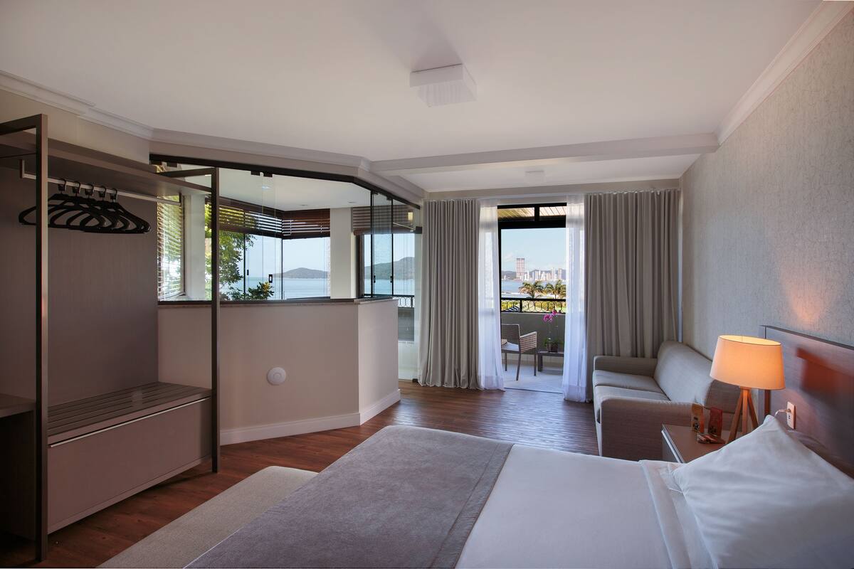 Ein Hotelzimmer mit Bett, Schreibtisch, Stuhl, Kleiderschrank und Blick auf die Stadt durch große Fenster.
