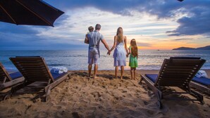 A family on a beach with a sunset view, wooden lounge chairs, and umbrellas. - Infinity Blue Resort & Spa (Balneário Camboriú)