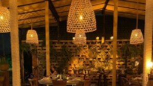 A restaurant with wooden tables set for dining, hanging pendant lights, and a stone wall in the background. - Infinity Blue Resort & Spa (Balneário Camboriú)