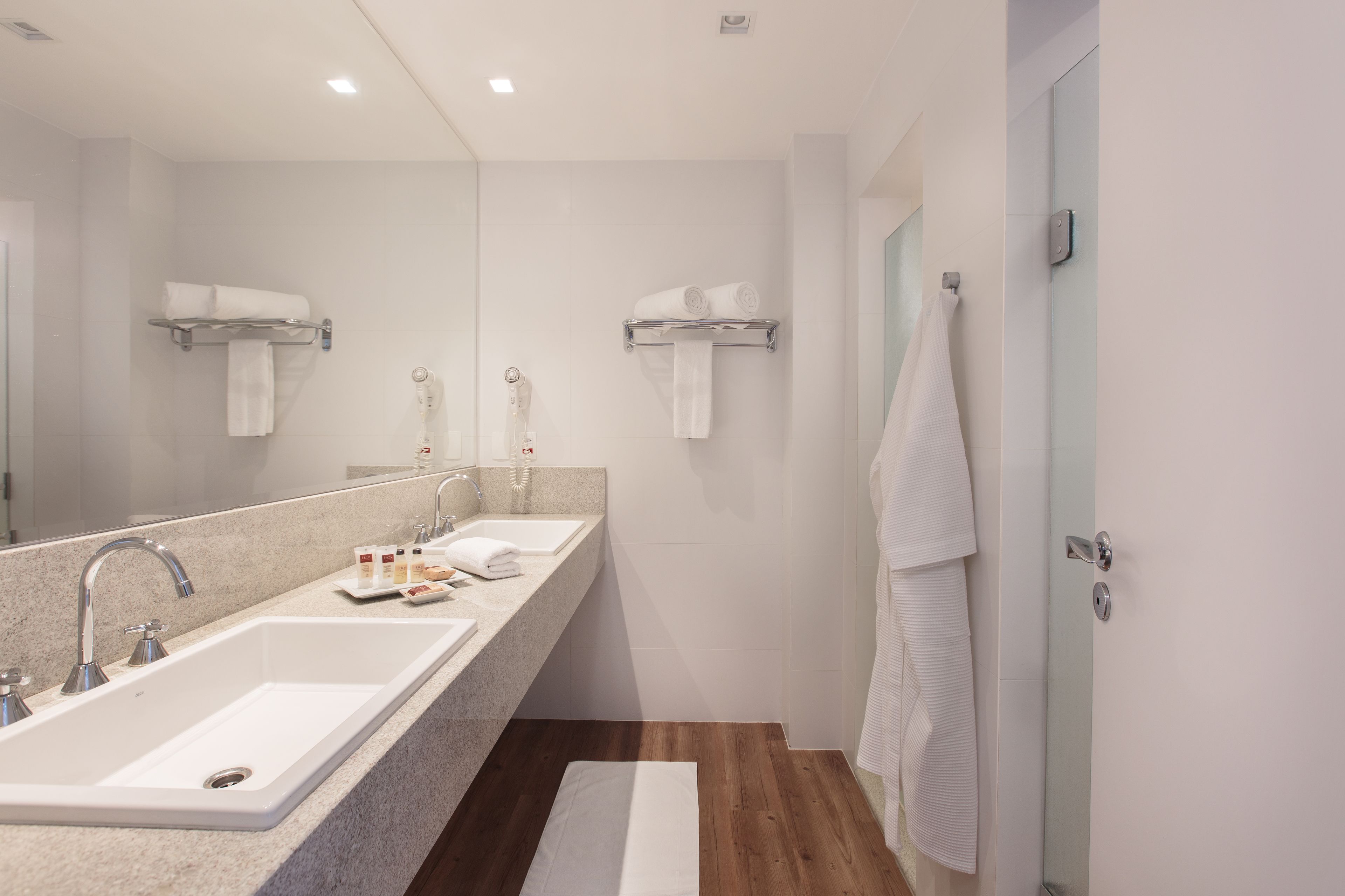 Un baño moderno con dos lavamanos, un espejo grande y suelo de madera.