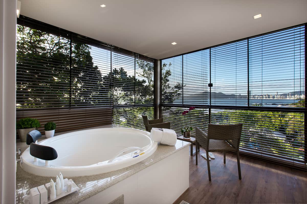 Ein modernes Badezimmer mit einer großen Badewanne, einer Sitzecke mit Stühlen und Blick auf ein Gewässer durch große Fenster.