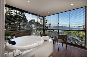 Ein modernes Badezimmer mit einer großen Badewanne, einer Sitzecke mit Stühlen und Blick auf ein Gewässer durch große Fenster.