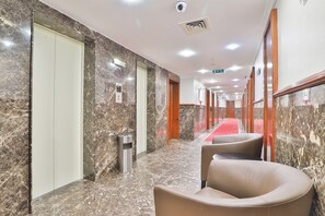 Pasillo de hotel con paredes de mármol, alfombra roja y un basurero.