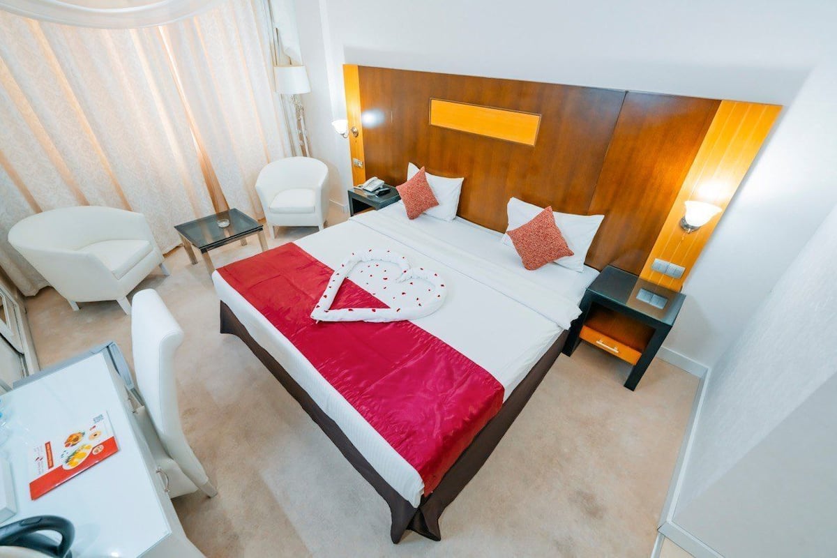 A hotel room with a large bed, two bedside tables, a desk with a chair, and a separate seating area with two chairs.