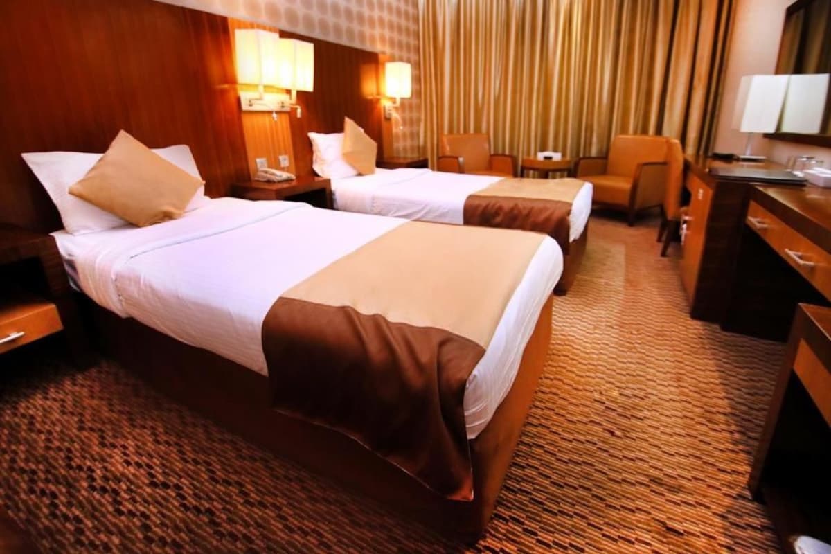 A hotel room with two beds, a desk, a chair, and a small table.