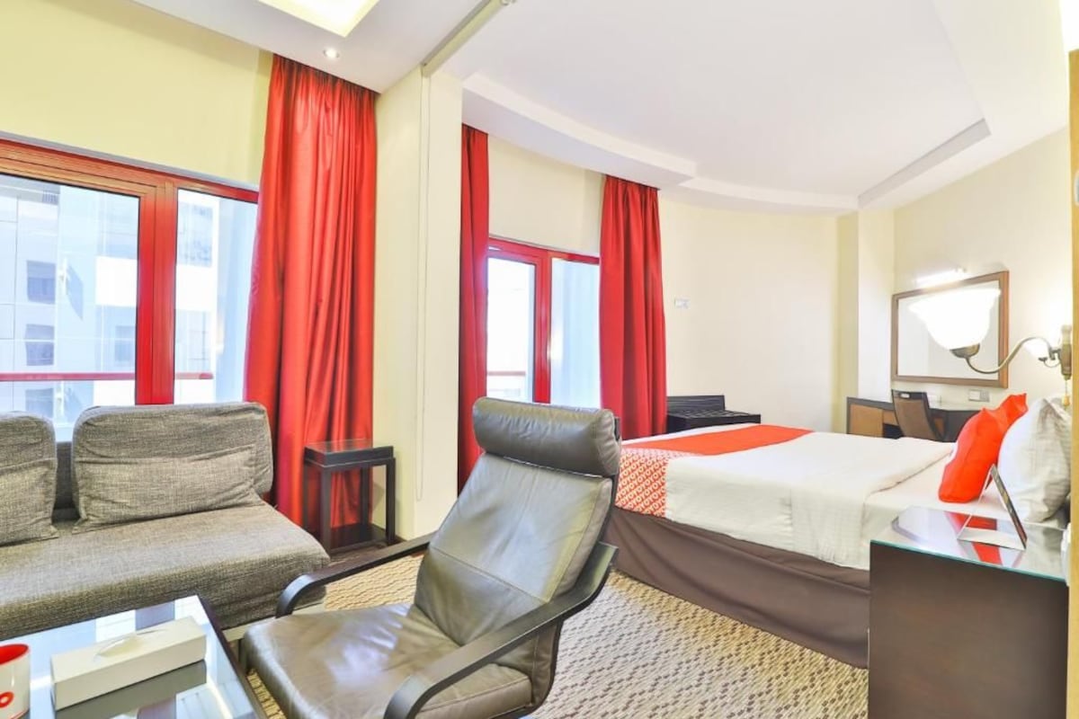 A hotel room with a bed, a sofa, a chair, a desk, and a mirror.