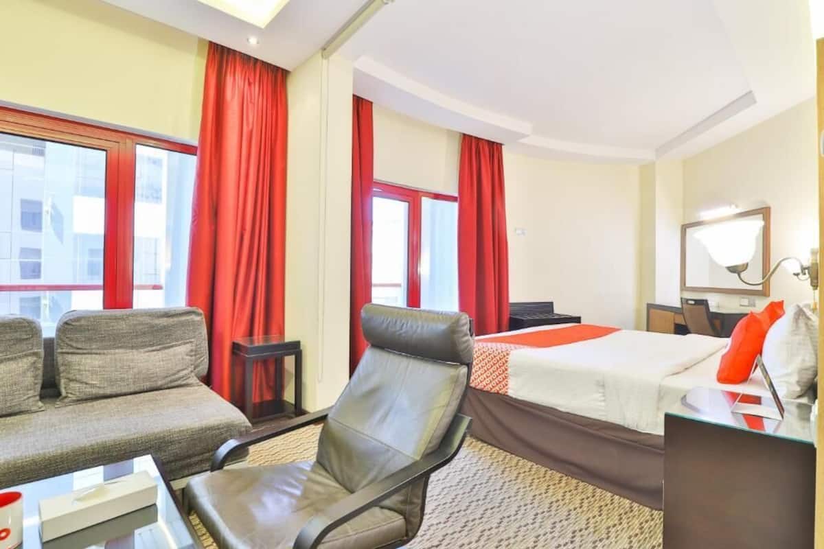 A hotel room with a bed, a sofa, a chair, a desk, and a mirror.