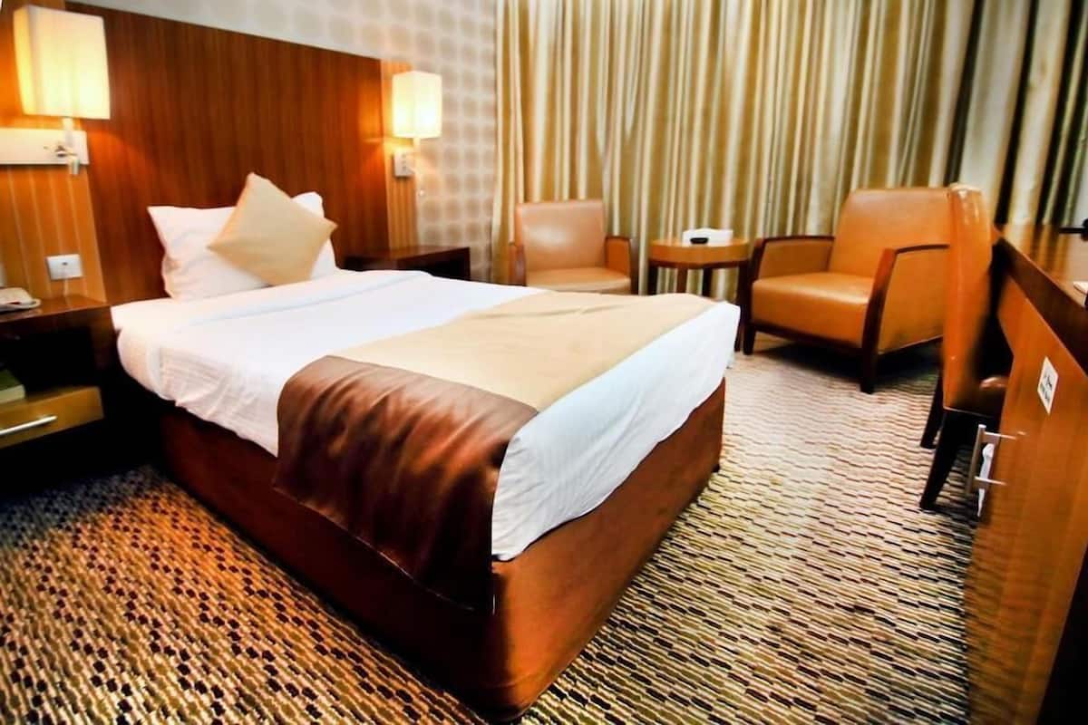 A hotel room with a large bed, two chairs, a small table, and a curtain.