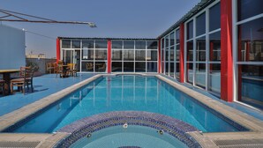 A swimming pool with a tiled edge, surrounded by red and white walls, and a seating area with chairs and a table. - Sun And Sands Downtown (Dubai)