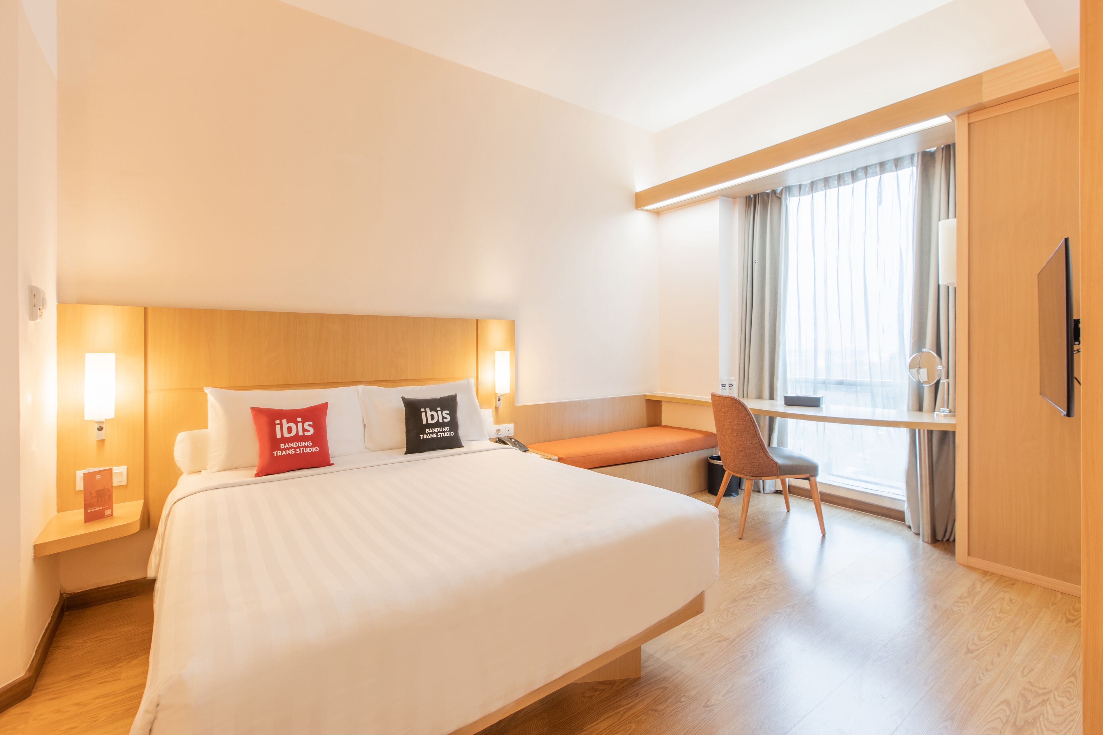 Quarto de hotel com uma cama grande, uma escrivaninha, uma cadeira e uma janela com cortinas.