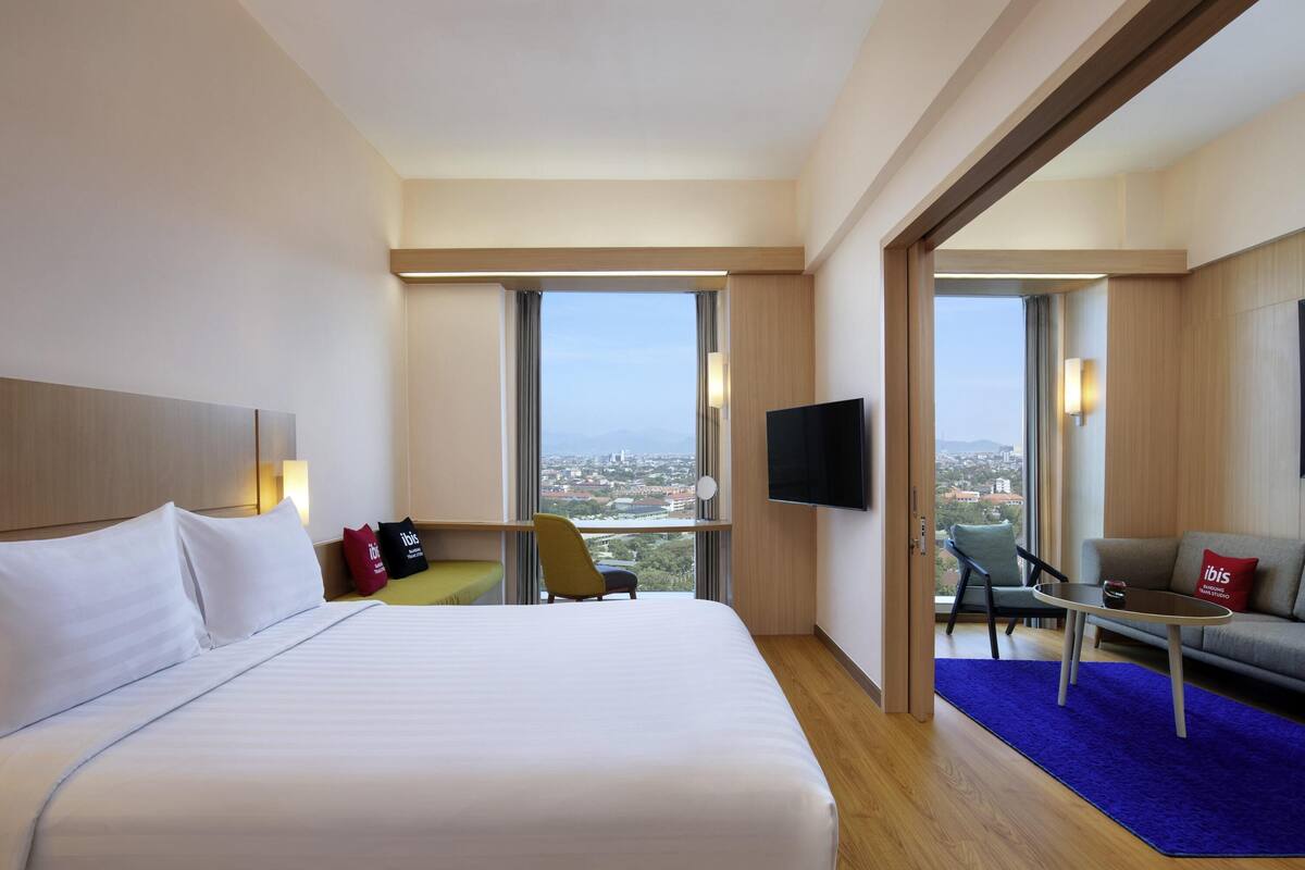 Ein Hotelzimmer mit einem großen Bett, einem Fernseher, einer Couch und Blick auf die Stadt.