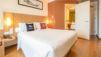 A hotel room with a large bed, two bedside lamps, a nightstand with a phone, and a door leading to a bathroom.
