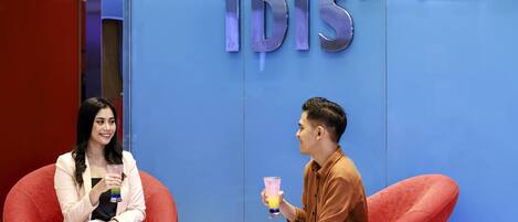 Dos personas sentadas en sillas rojas frente a una pared azul con el logo 'ibis'.