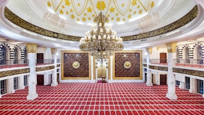A grand hall with a red carpet, ornate chandeliers, and intricate wall designs.