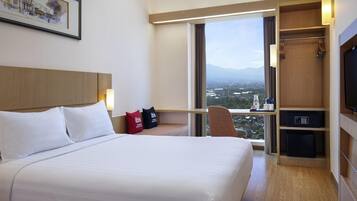 Habitación de hotel con una cama grande, un escritorio con silla, un televisor y vistas a un paisaje urbano a través de un ventanal amplio.