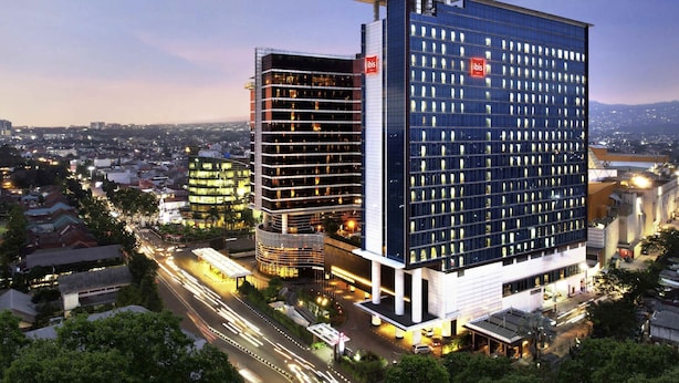 A modern hotel with a prominent glass facade, multiple floors, and a rooftop terrace.