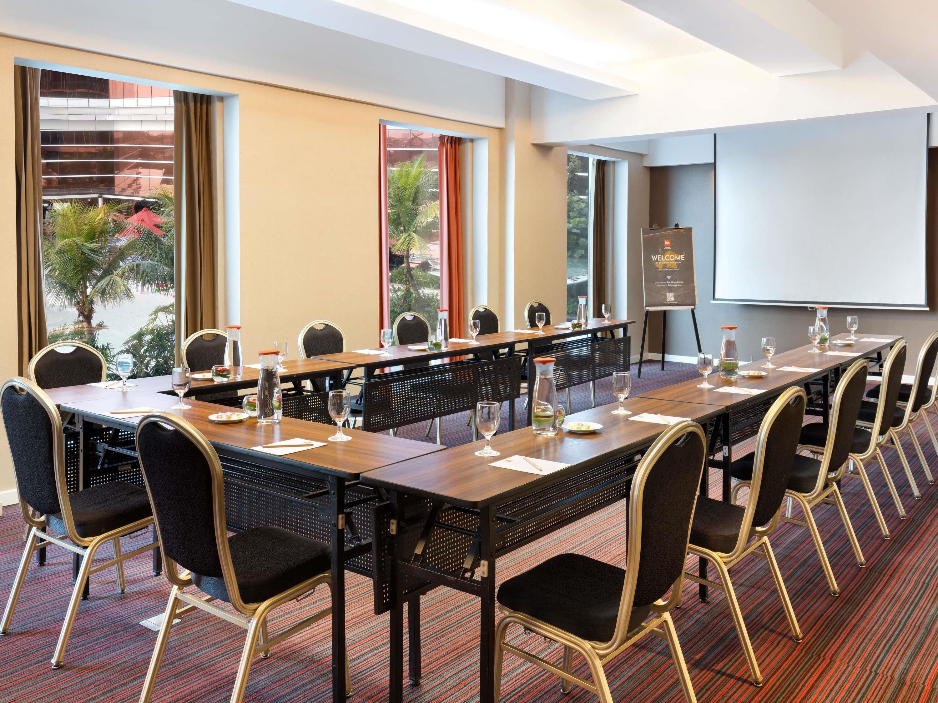Une salle de conférence avec une longue table, des chaises, un écran de projection et un panneau d’accueil.