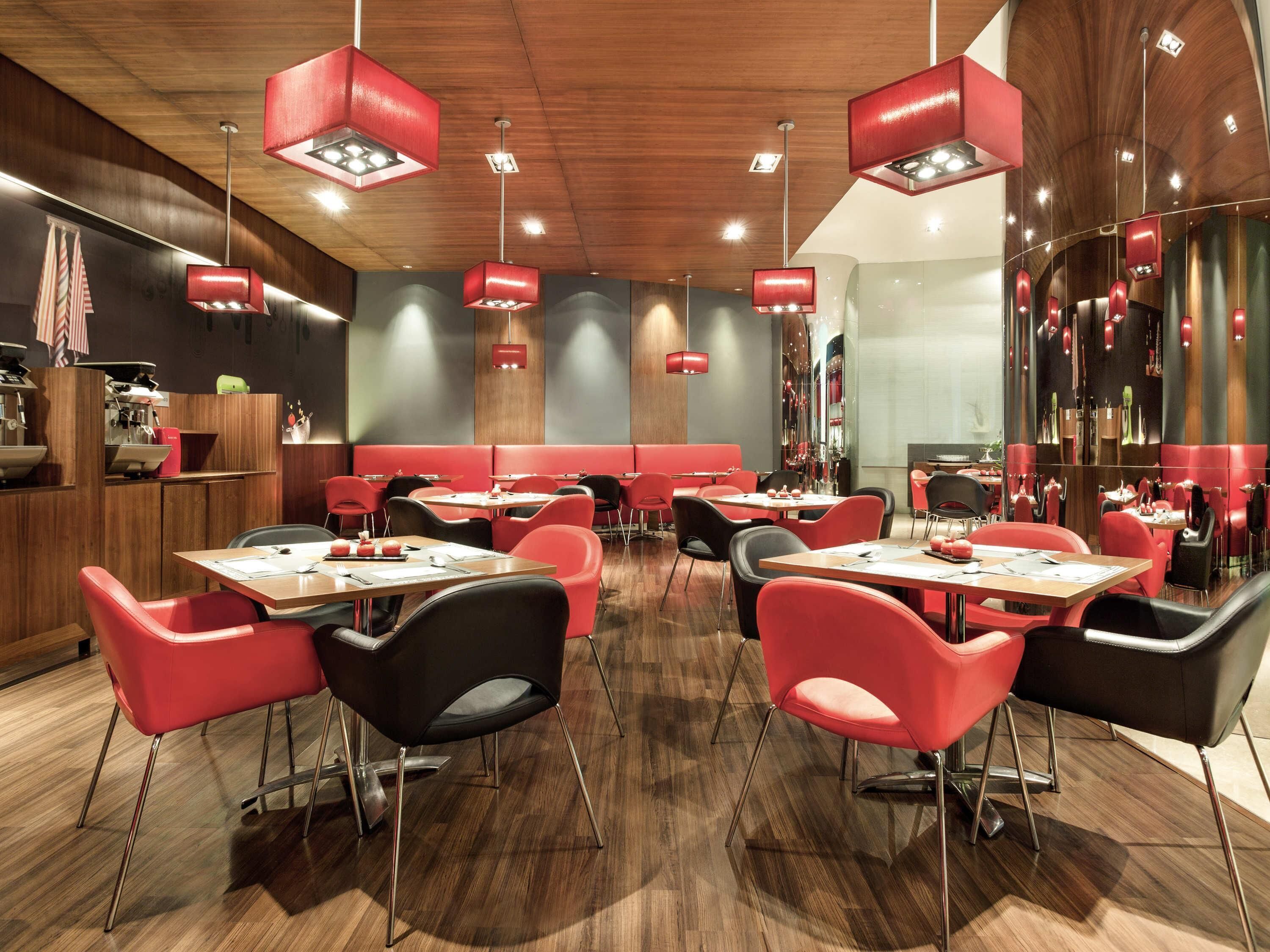 Een modern restaurantinterieur met rode en zwarte stoelen, houten vloeren en rode hanglampen.