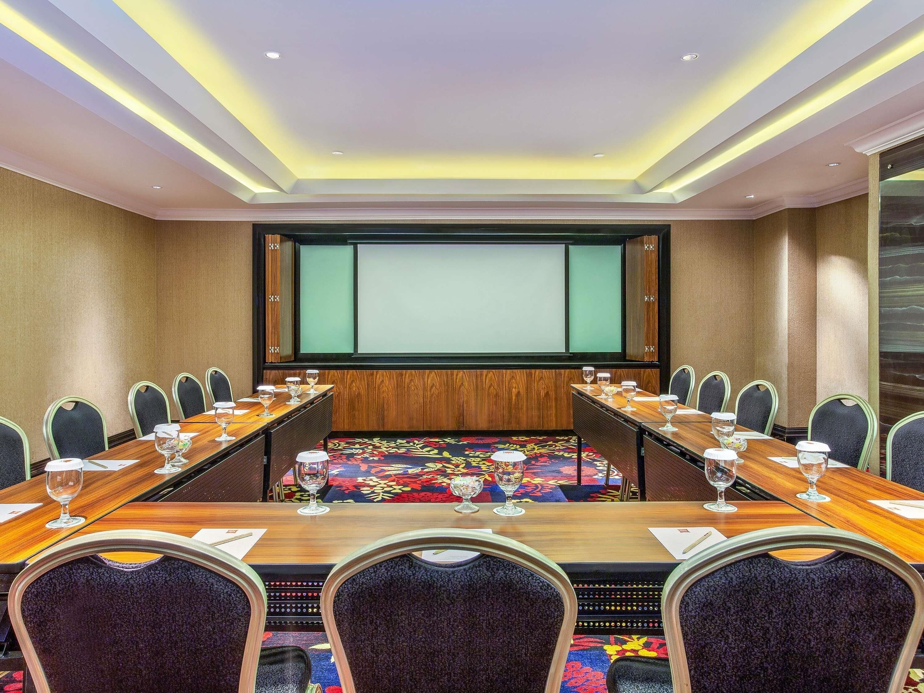 A conference room with a long table, chairs, a projector screen, and a carpeted floor.