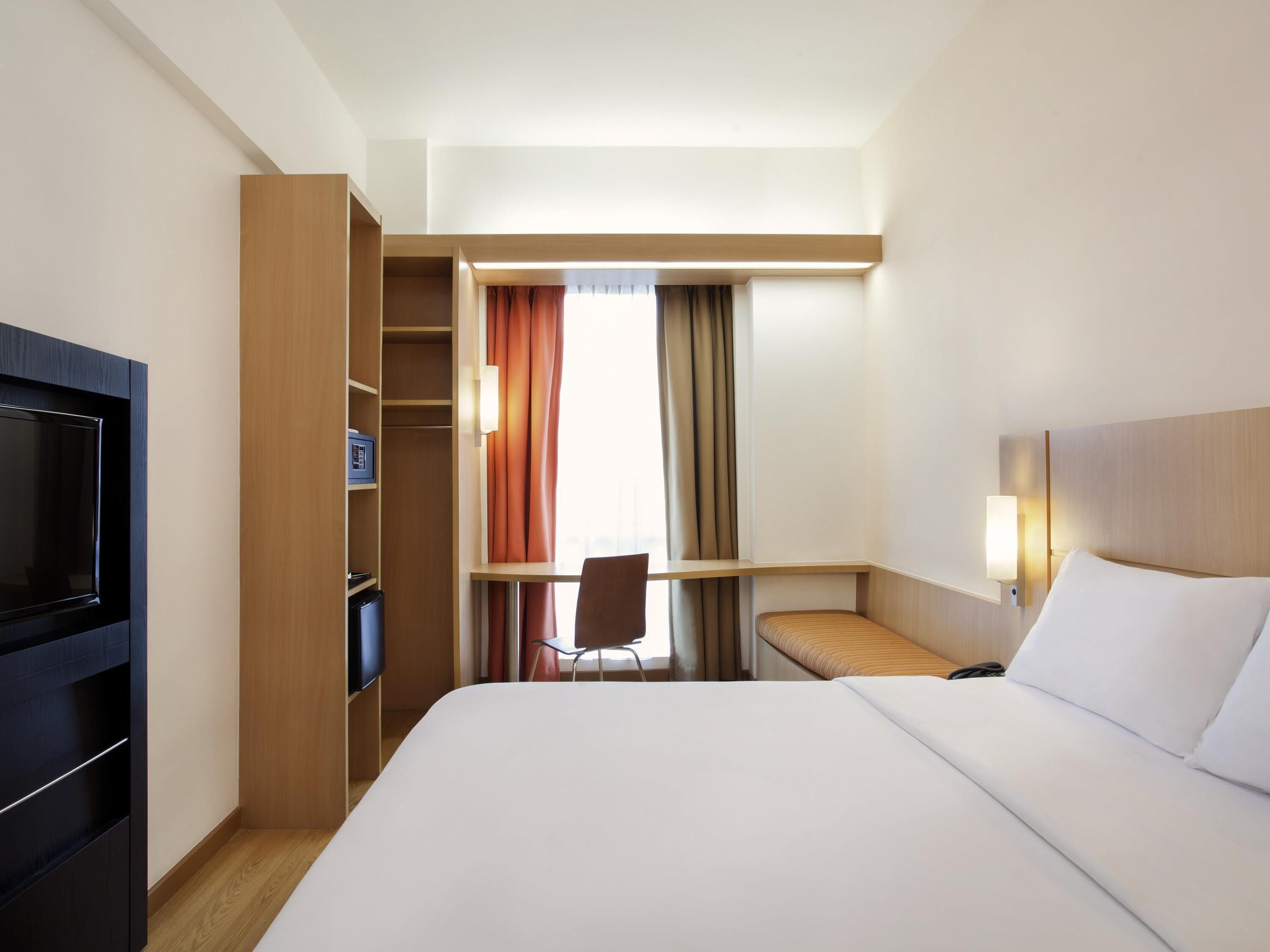 Een hotelkamer met een bed, een televisie, een bureau en een stoel.