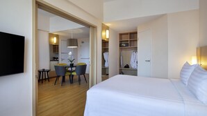 A hotel room with a large bed, a dining area with a table and chairs, a walk-in closet, and a TV mounted on the wall.