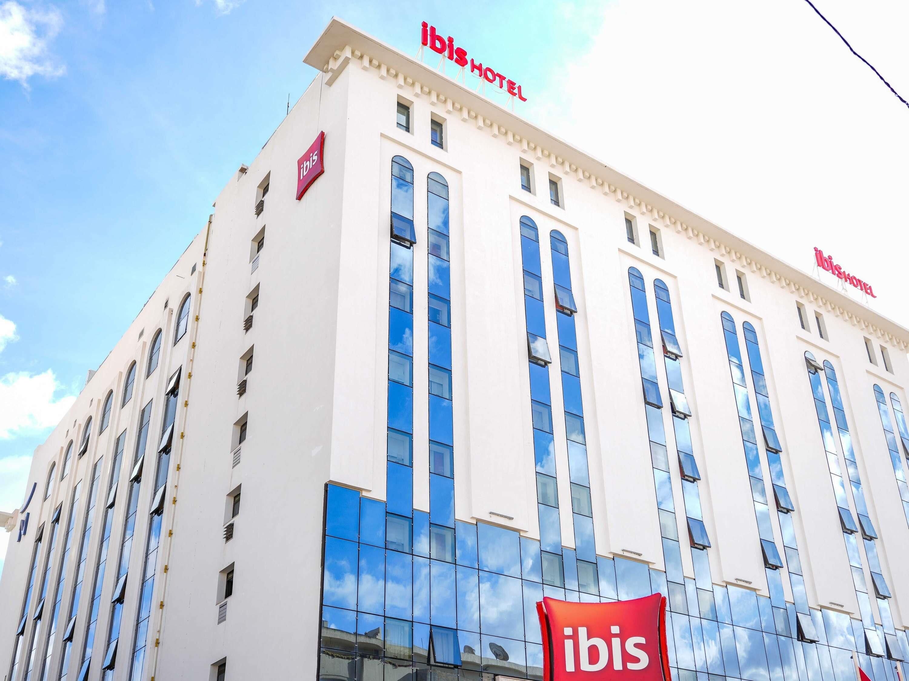 Ein modernes Hotelgebäude, auf dessen Fassade das 'ibis'-Logo gut sichtbar ist.