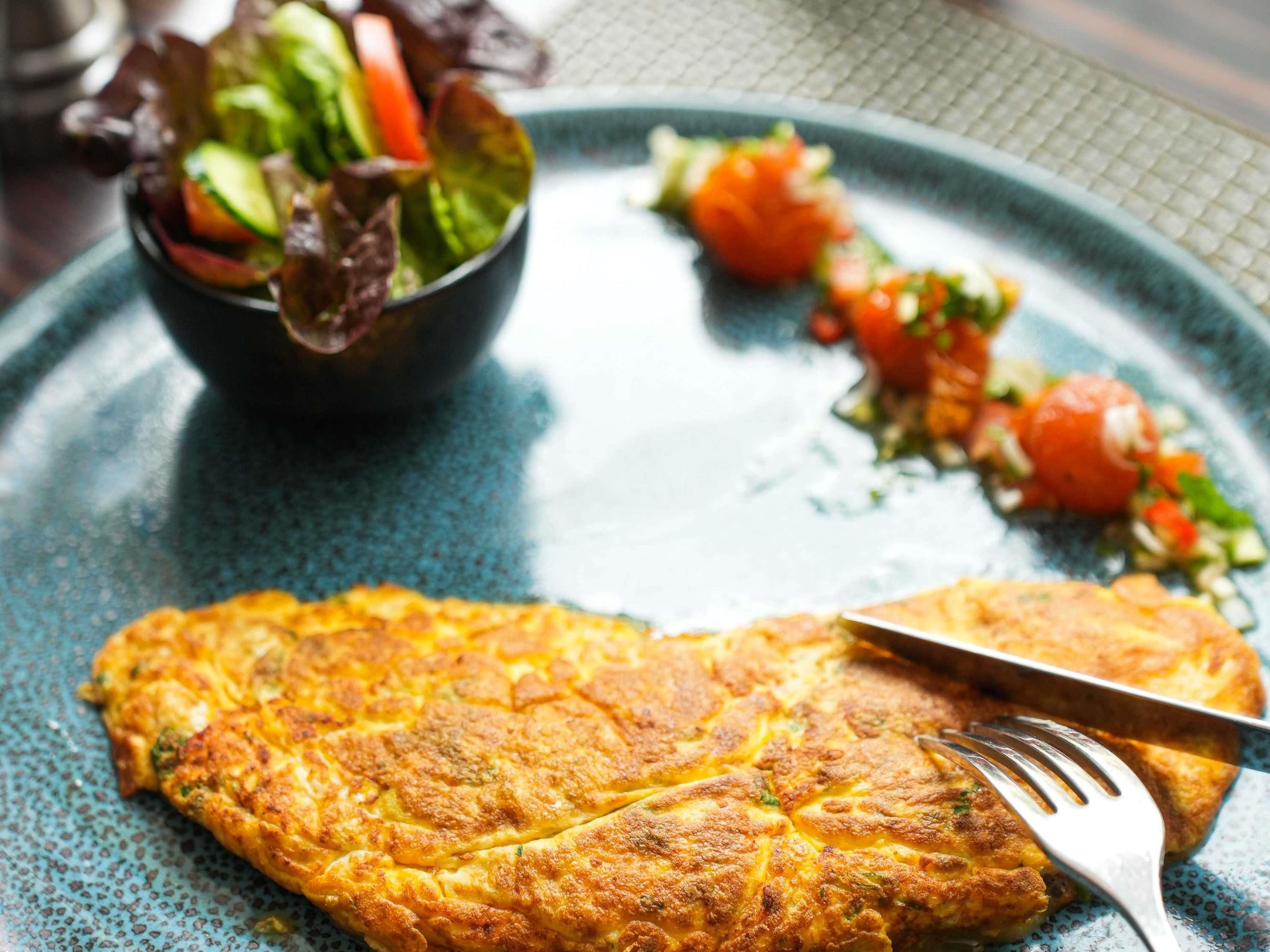 Un plato con una tortilla dorada, una ensalada pequeña y un acompañamiento a base de tomate.
