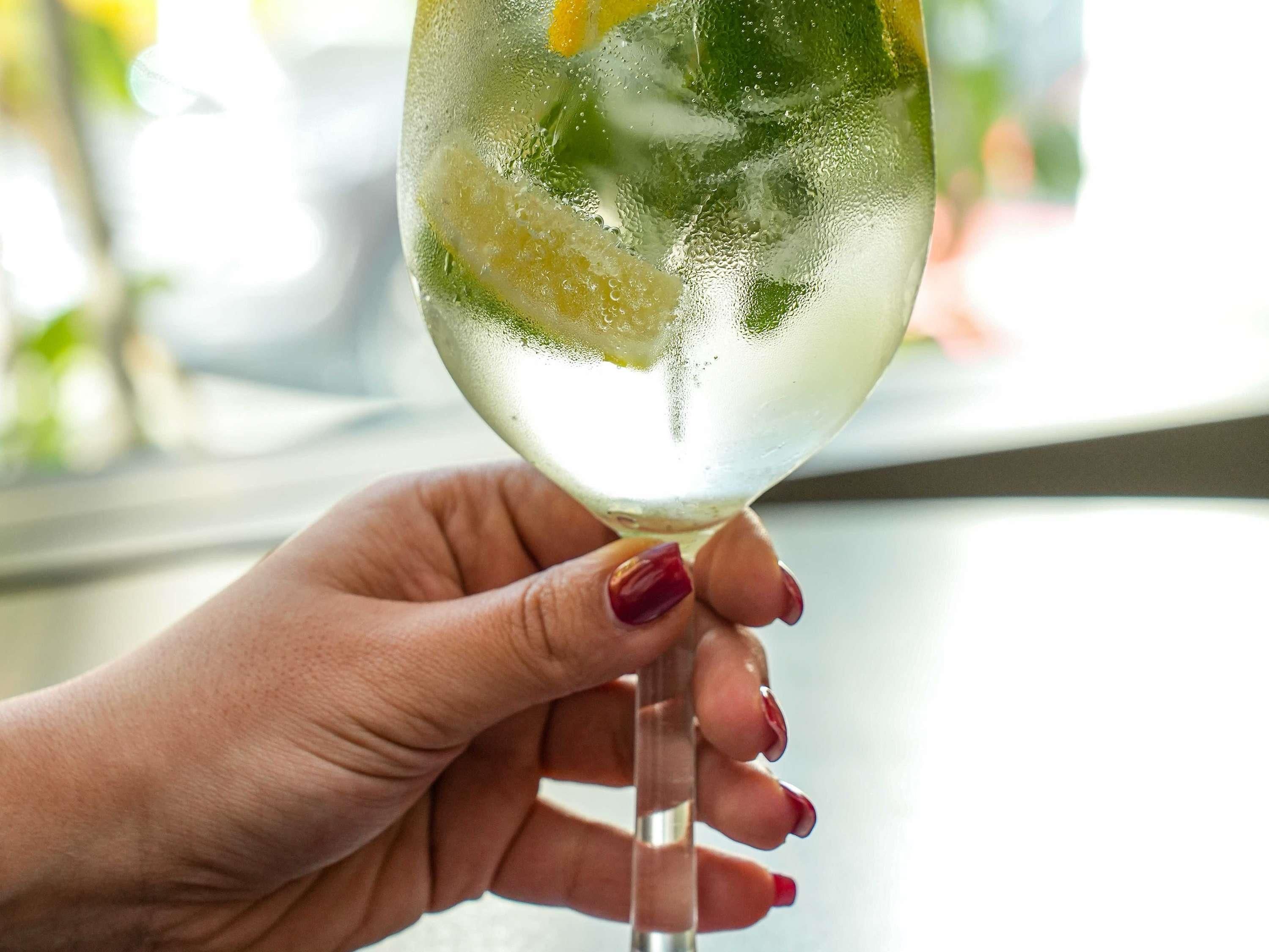 A hand holding a glass with a beverage and ice cubes.