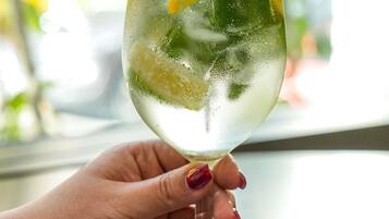 A hand holding a glass with a beverage and ice cubes.