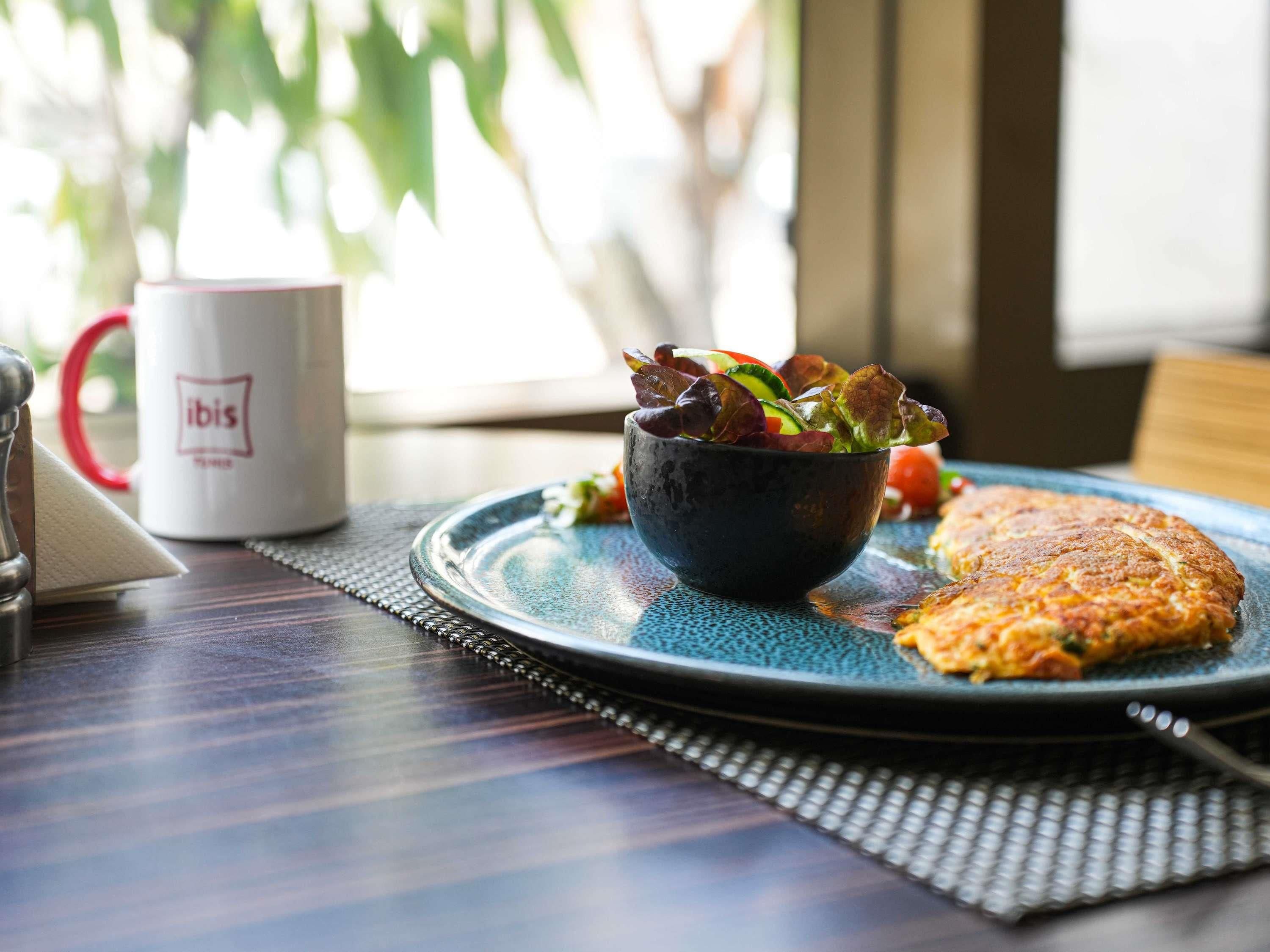 Un desayuno con un plato de comida, un bol de ensalada y una taza de café sobre una mesa.