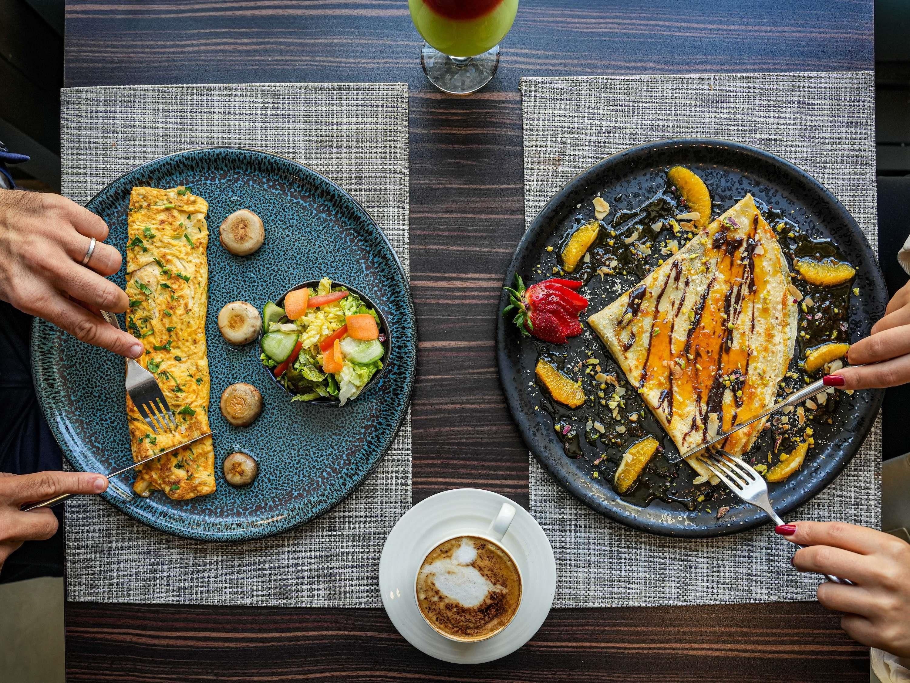Una mesa de comedor con dos platos de comida, una taza de café y un vaso de bebida.