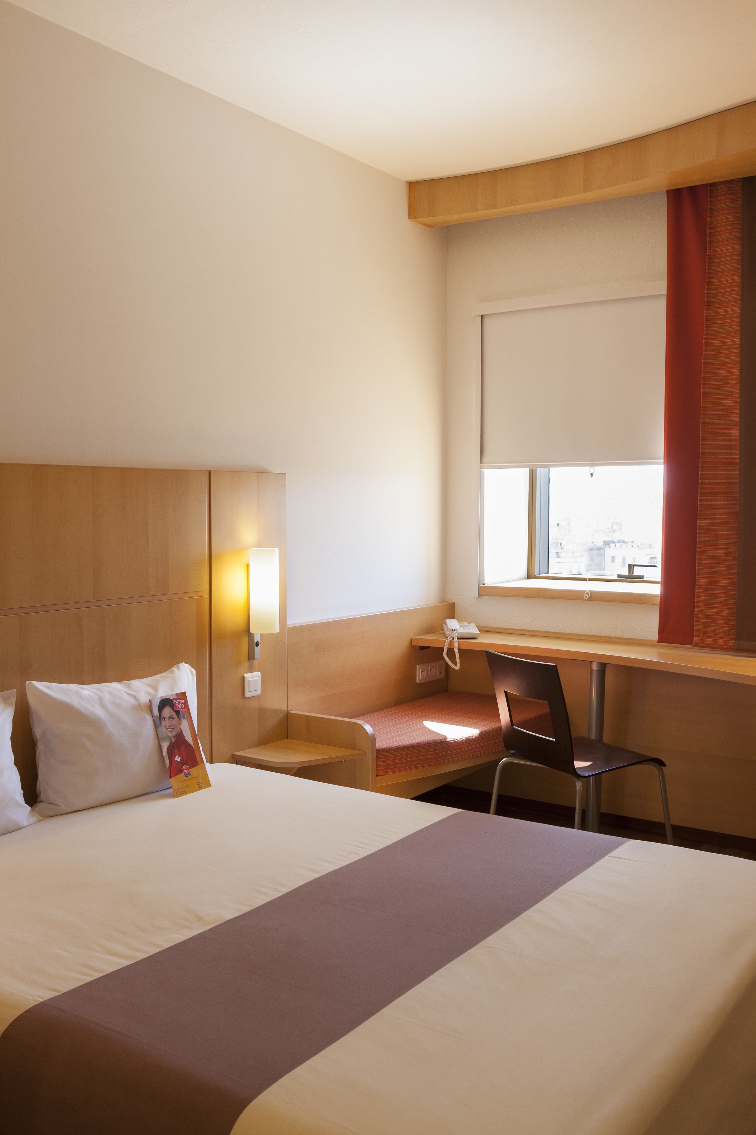 Une chambre d’hôtel équipée d’un lit, d’un bureau, d’une chaise, d’une fenêtre donnant sur un paysage agréable et d’un téléphone fixé au mur.