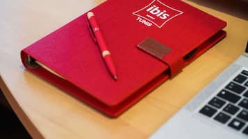 Un cuaderno rojo con la marca ibis Hotels Túnez, un bolígrafo y una computadora portátil sobre una superficie de madera.