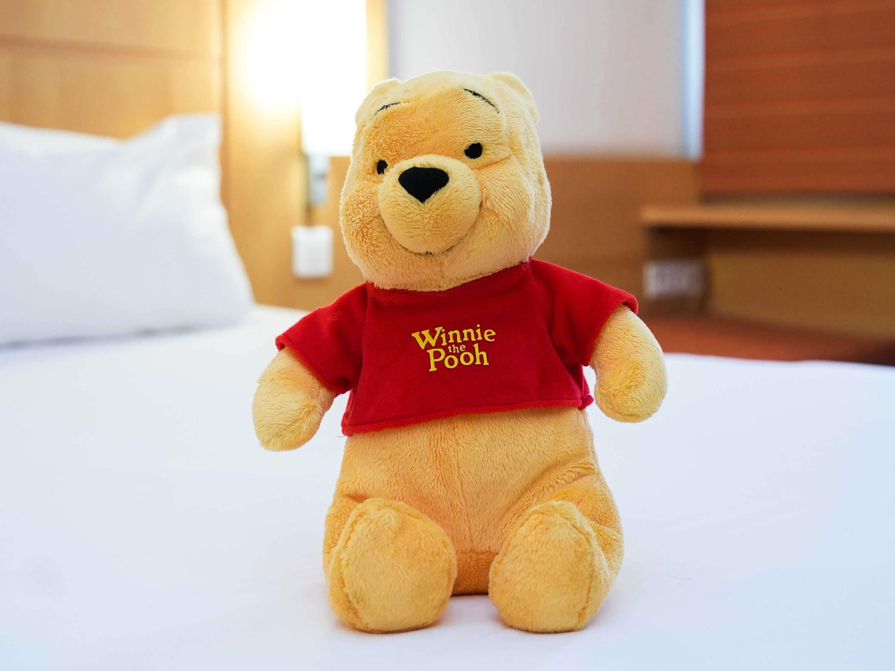 A plush Winnie the Pooh toy on a bed in a hotel room.