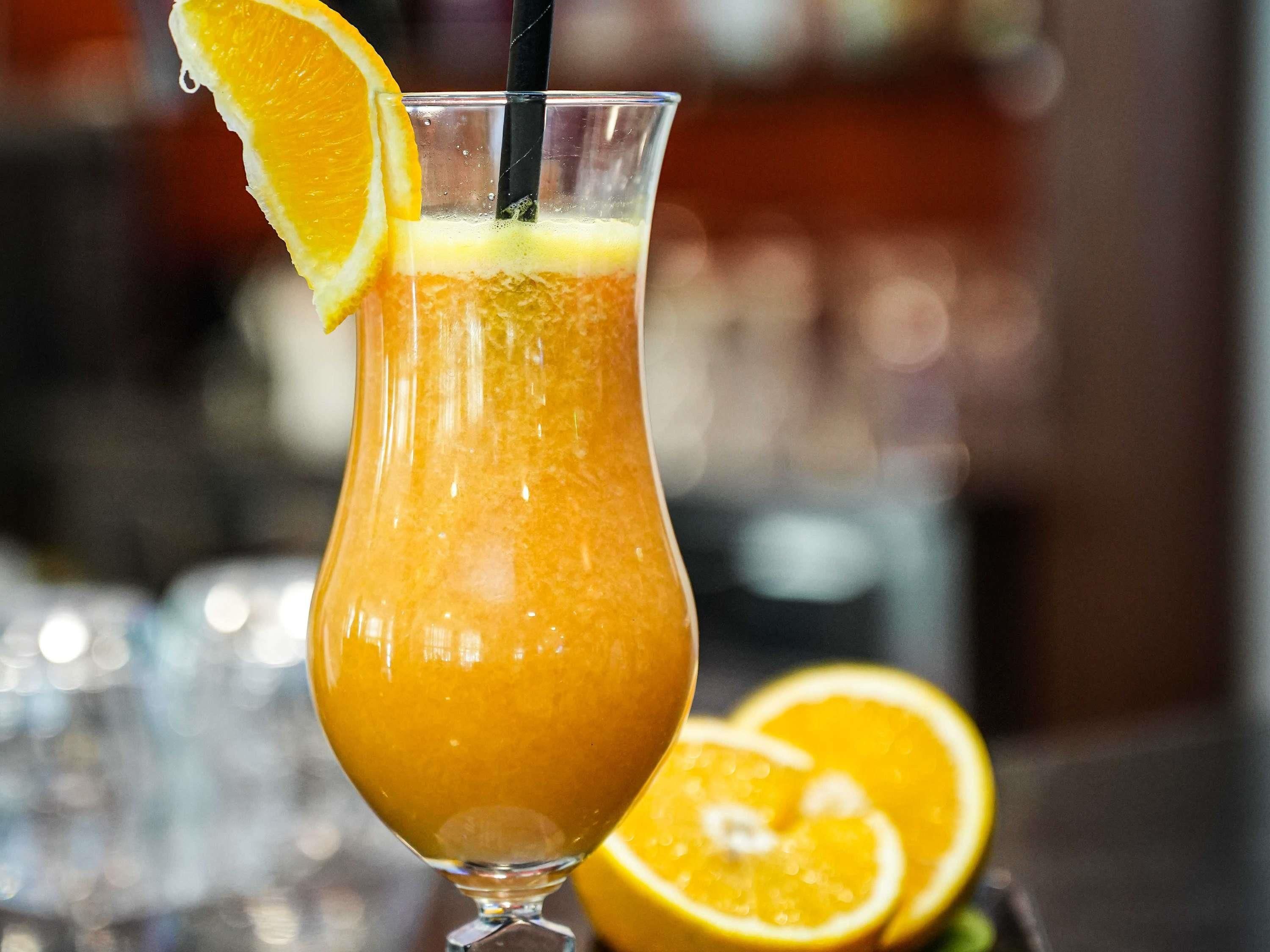 A tall glass with a thick orange beverage, a slice of orange on the rim, and a straw.