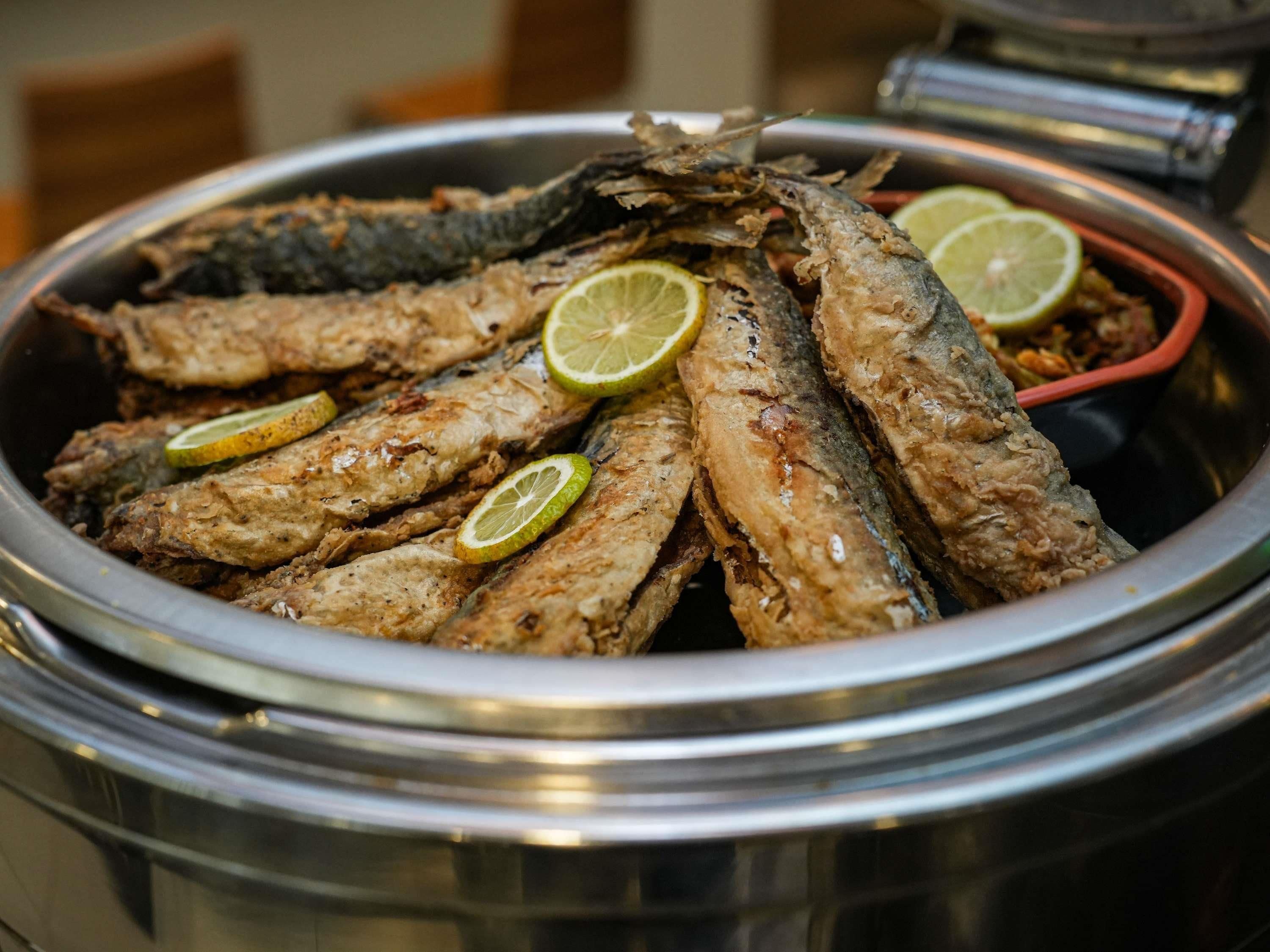 Un contenedor metálico grande lleno de pescado frito, adornado con rodajas de limón.