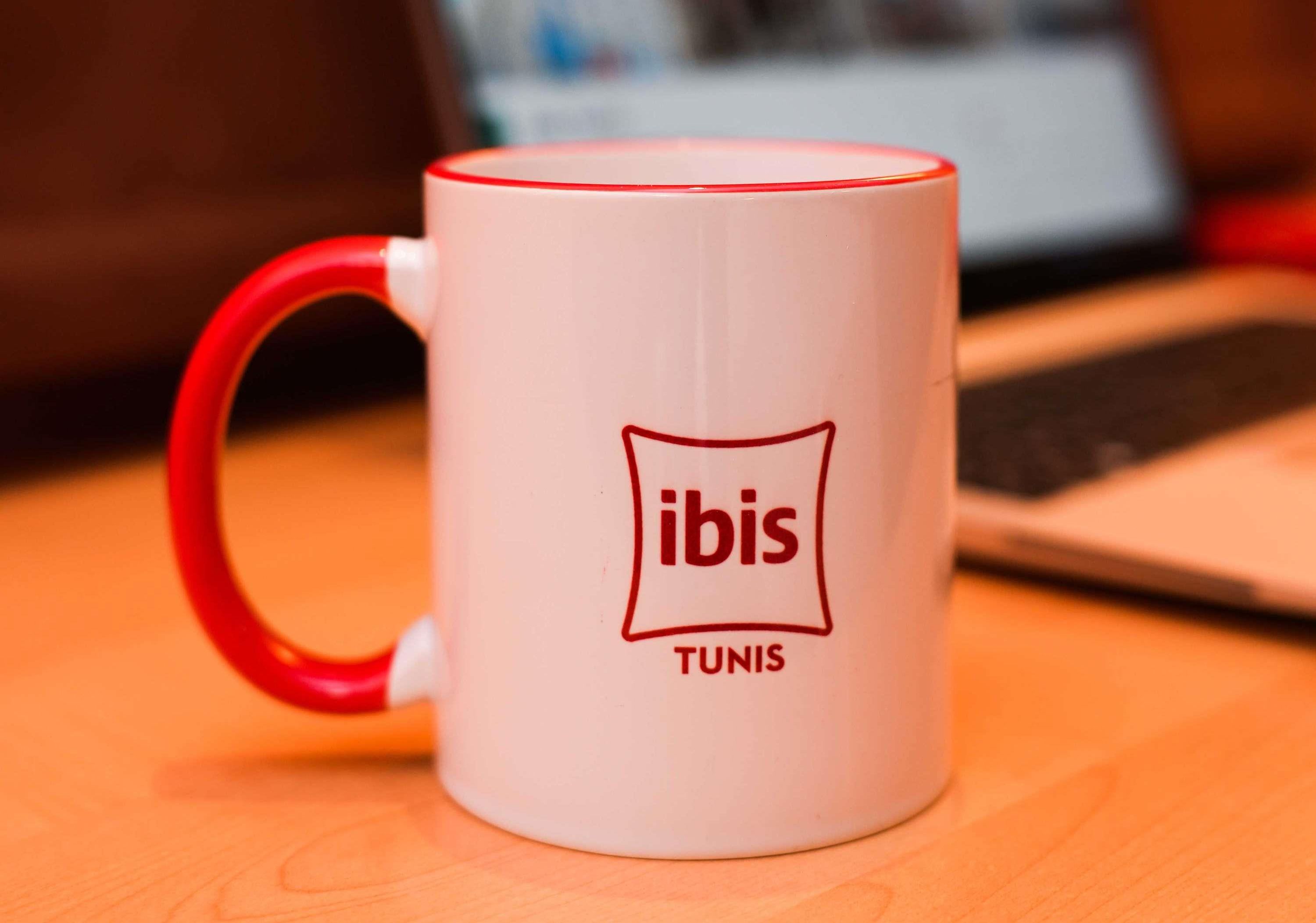Eine weiße Tasse mit rotem Henkel und dem Schriftzug "ibis" und "Tunis".
