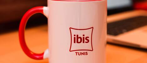 Eine weiße Tasse mit rotem Henkel und dem Schriftzug "ibis" und "Tunis".