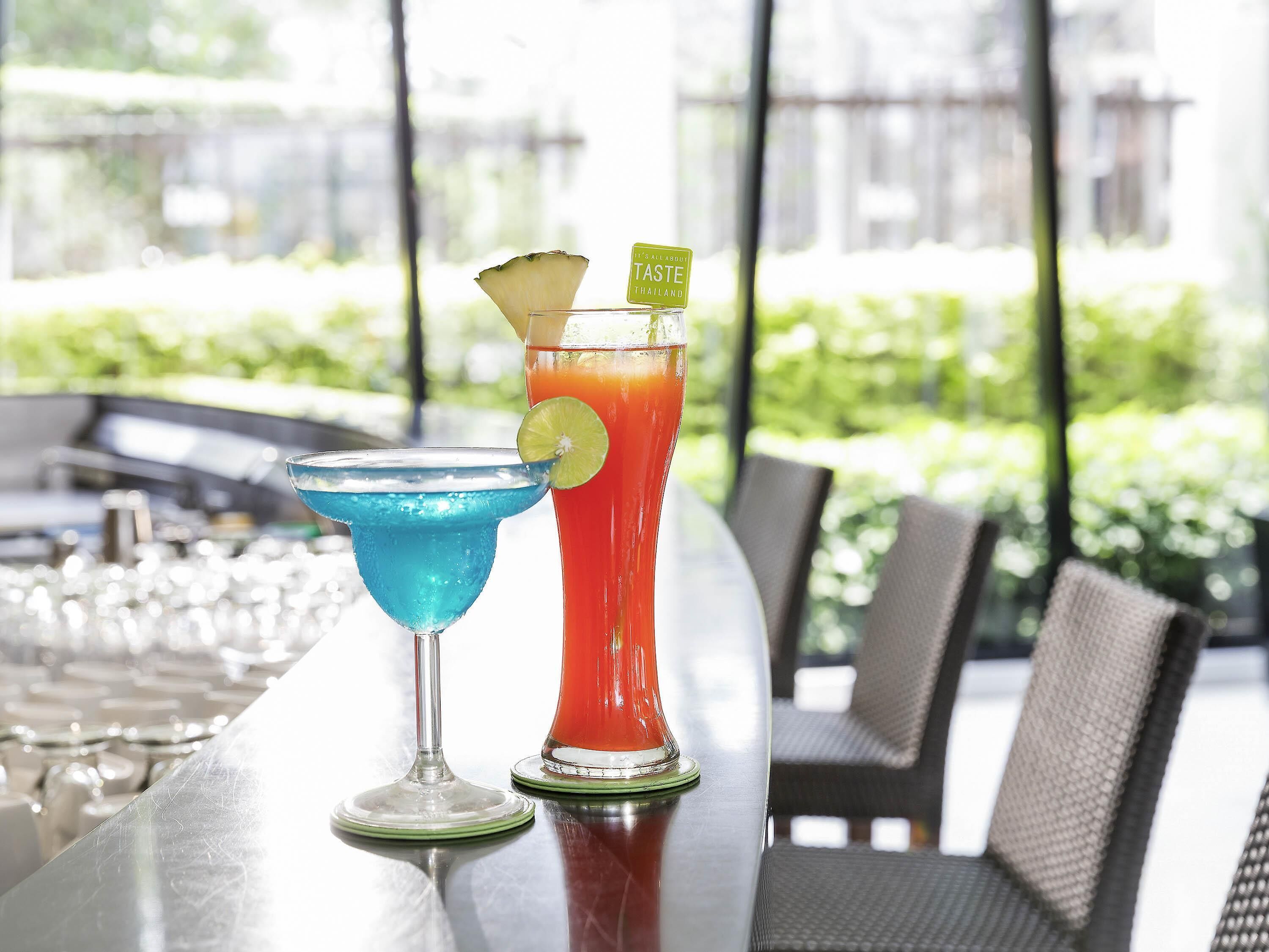 Twee cocktails op een bartafel met uitzicht op groen.